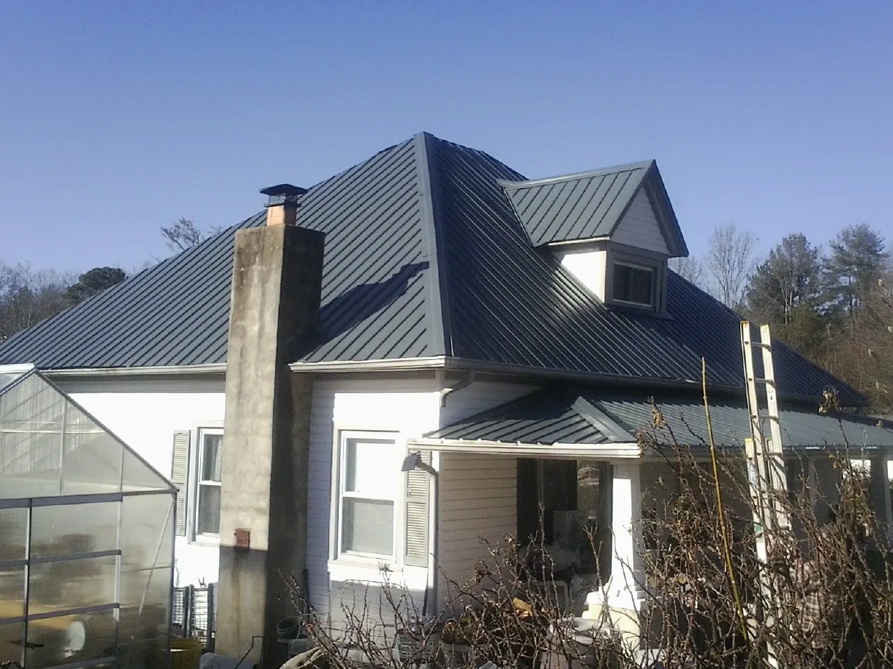 Dark blue standing seam metal roof on a white farmhouse with dormer — Slate & Tile Roof Repair by Roofing Brothers in Pepperell