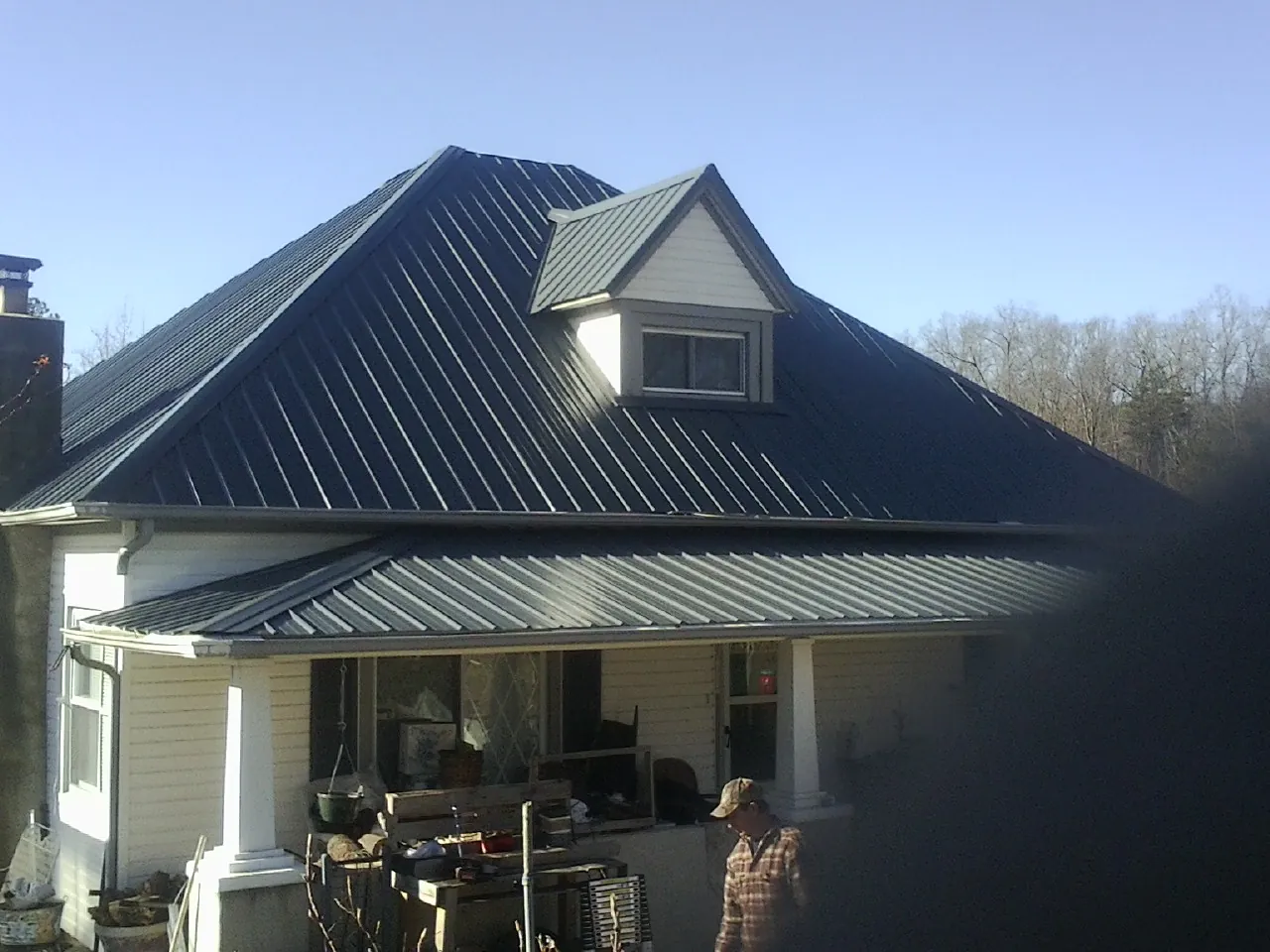 Dark blue standing seam metal roof with a dormer above a front porch in Pepperell