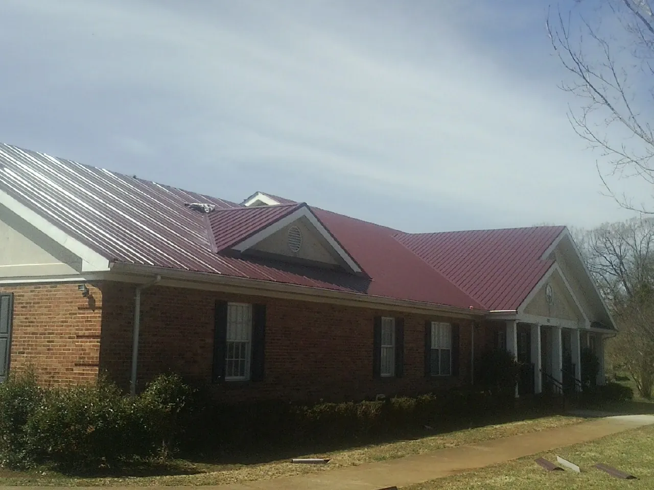 Red metal roof with gabled entries on a long brick building, from a Hail Damage Roof Repair job in Pepperell