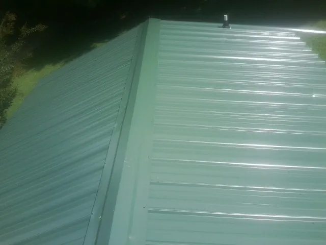 New green metal panels meeting at the ridge of a roof — Flat Roof Repair work by our crew in Pepperell