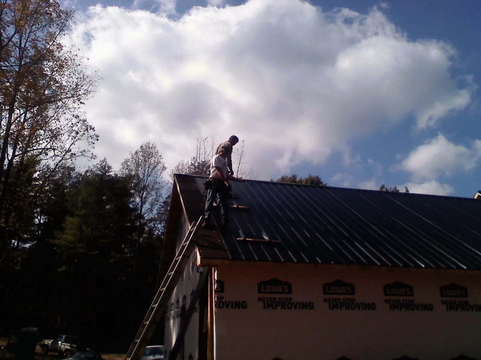 Roofer fastening dark metal panels high against a cloudy sky, from a Roof Inspection job in Pepperell