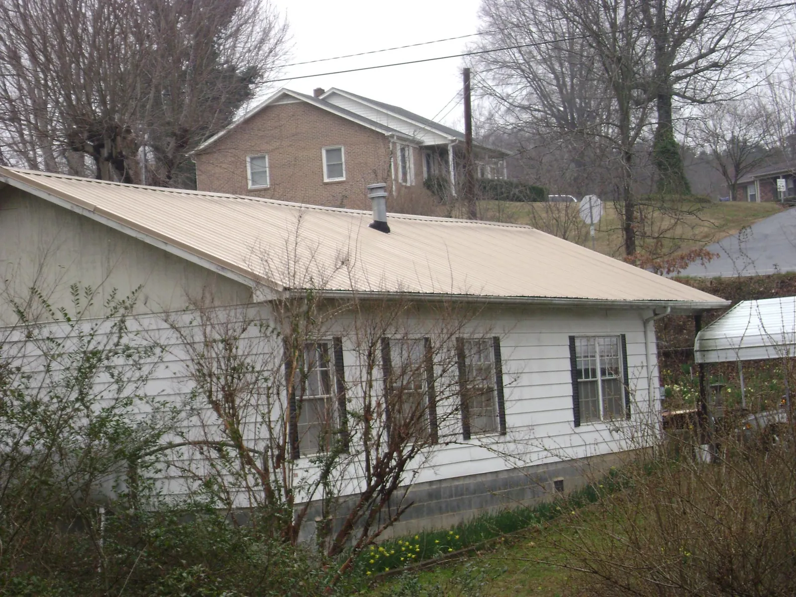 Tan metal roof on a white sided house set into a hillside — Commercial Roofing by Roofing Brothers in Pepperell